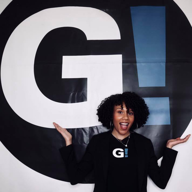 Smiling young black woman against a backdrop with the Girls Be Heard logo